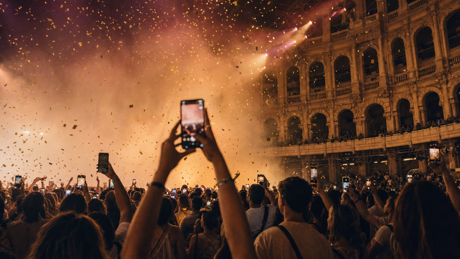 Público con los brazos en alto y móviles encendidos bajo una lluvia de confeti en un gran concierto