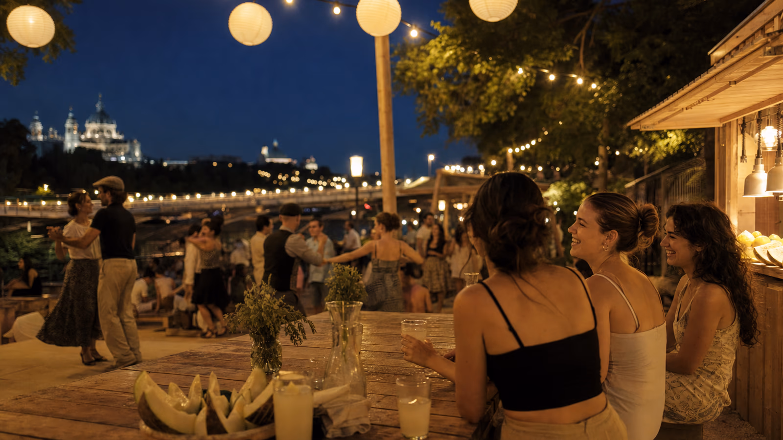 Riverside verbena in Madrid Rio: friends with lemonade and melon while couples dance under paper lanterns