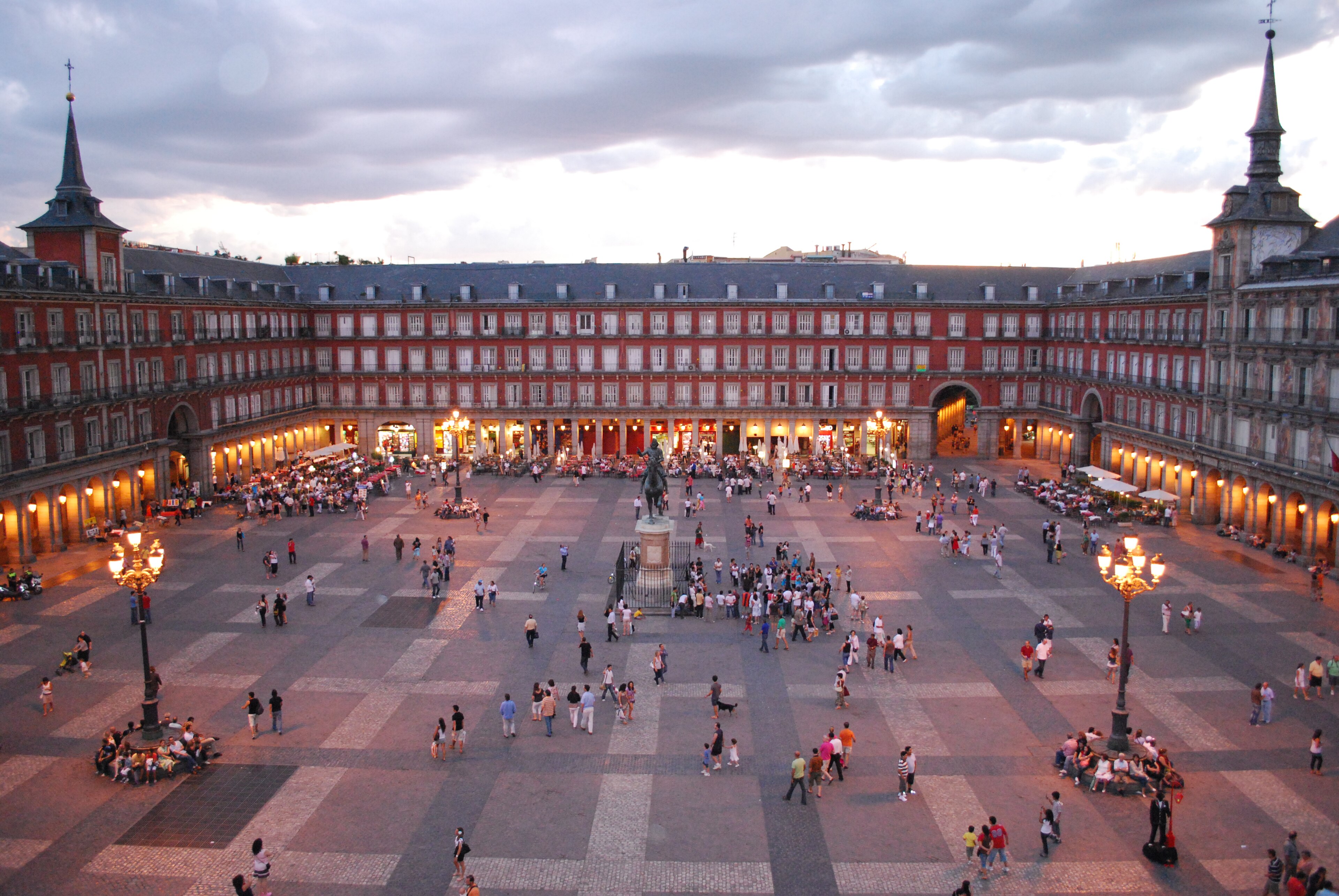 Plaza Mayor in Madrid at sunset, with people on the square and lights on